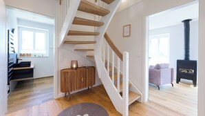 Un interior moderno con una escalera de madera, una estufa de leña negra y un rincón de estar acogedor.