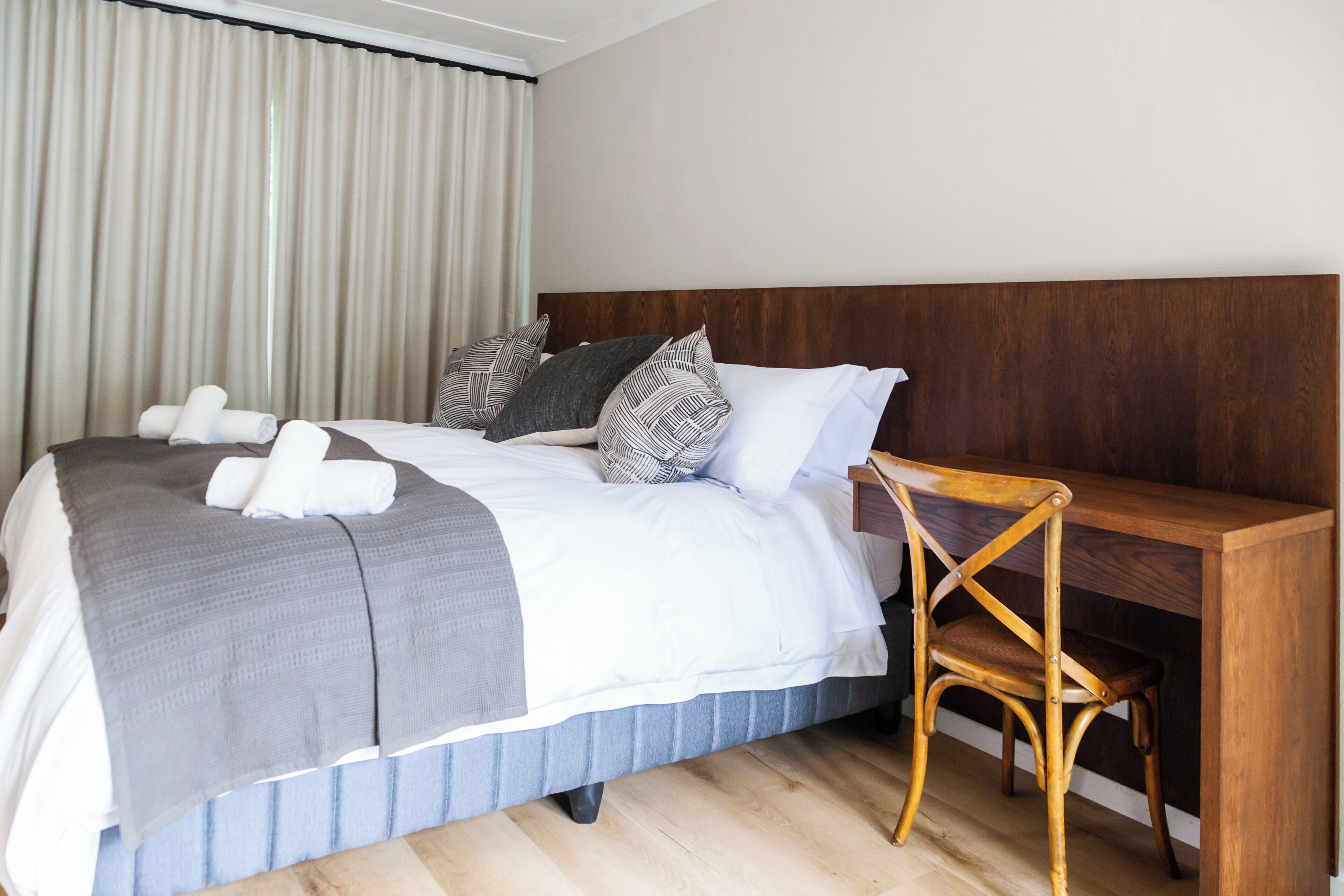 Una cama bien hecha con edredón gris y blanco, un cabecero de madera y un escritorio de madera con una silla.