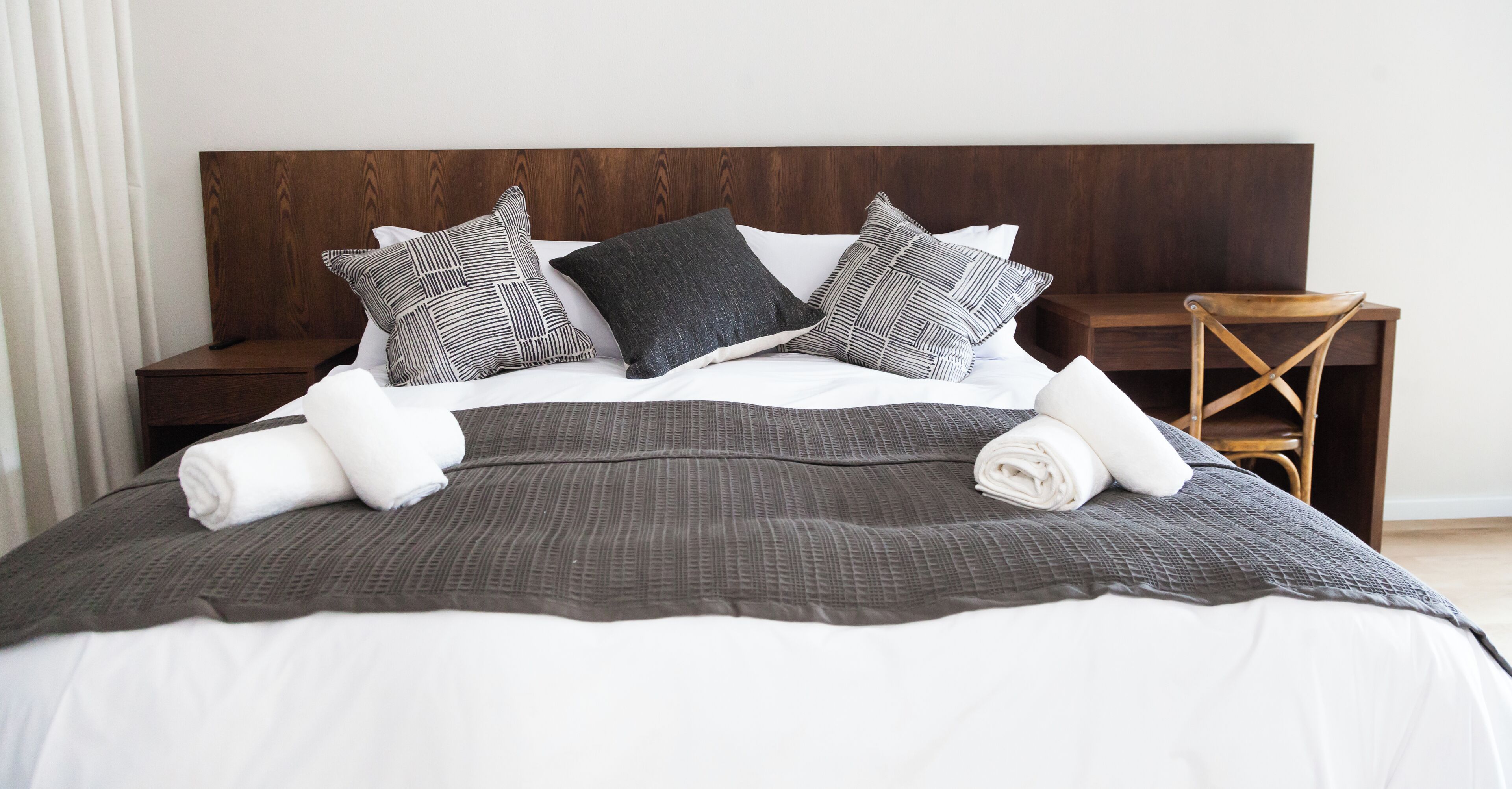 Una cama bien hecha con una colcha gris oscuro, almohadas blancas y un cabecero de madera.