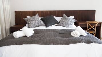Una cama bien hecha con una colcha gris oscuro, almohadas blancas y un cabecero de madera.
