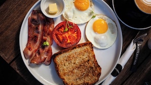 Un plato de desayuno con tocino, huevos, tostadas y tomate.