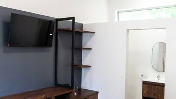 Habitación de hotel con cama, escritorio con silla, televisor montado en la pared, baño con espejo y ventana.