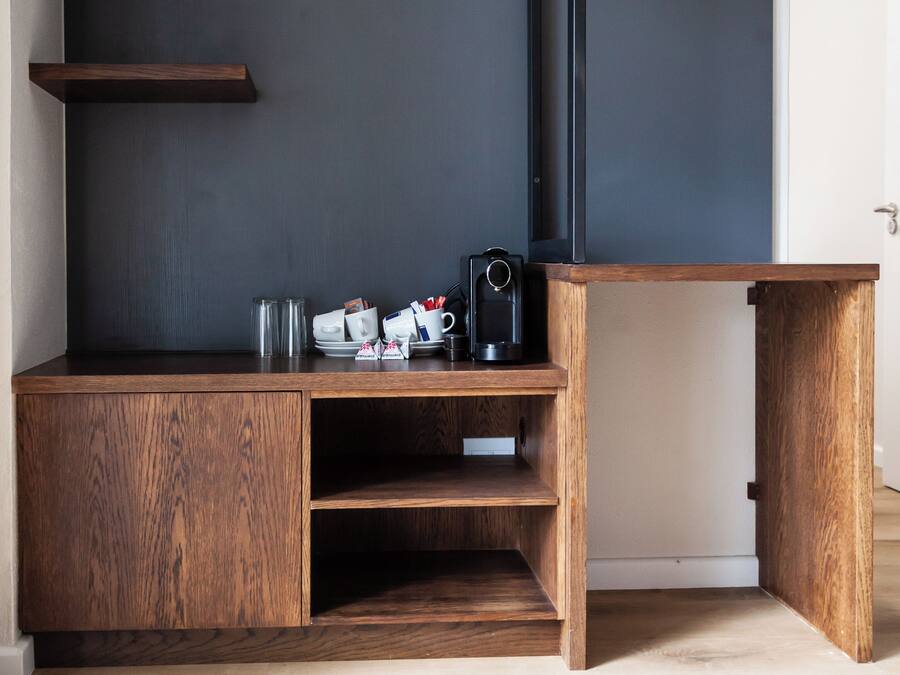 A wooden desk with a dark wall behind it, containing a coffee maker, cups, and a small box.