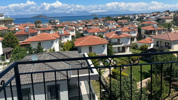 A coastal residential area with houses featuring red-tiled roofs, a clear blue sky, and a distant view of the sea. - Ege Vadi Otel (Ayvalik)