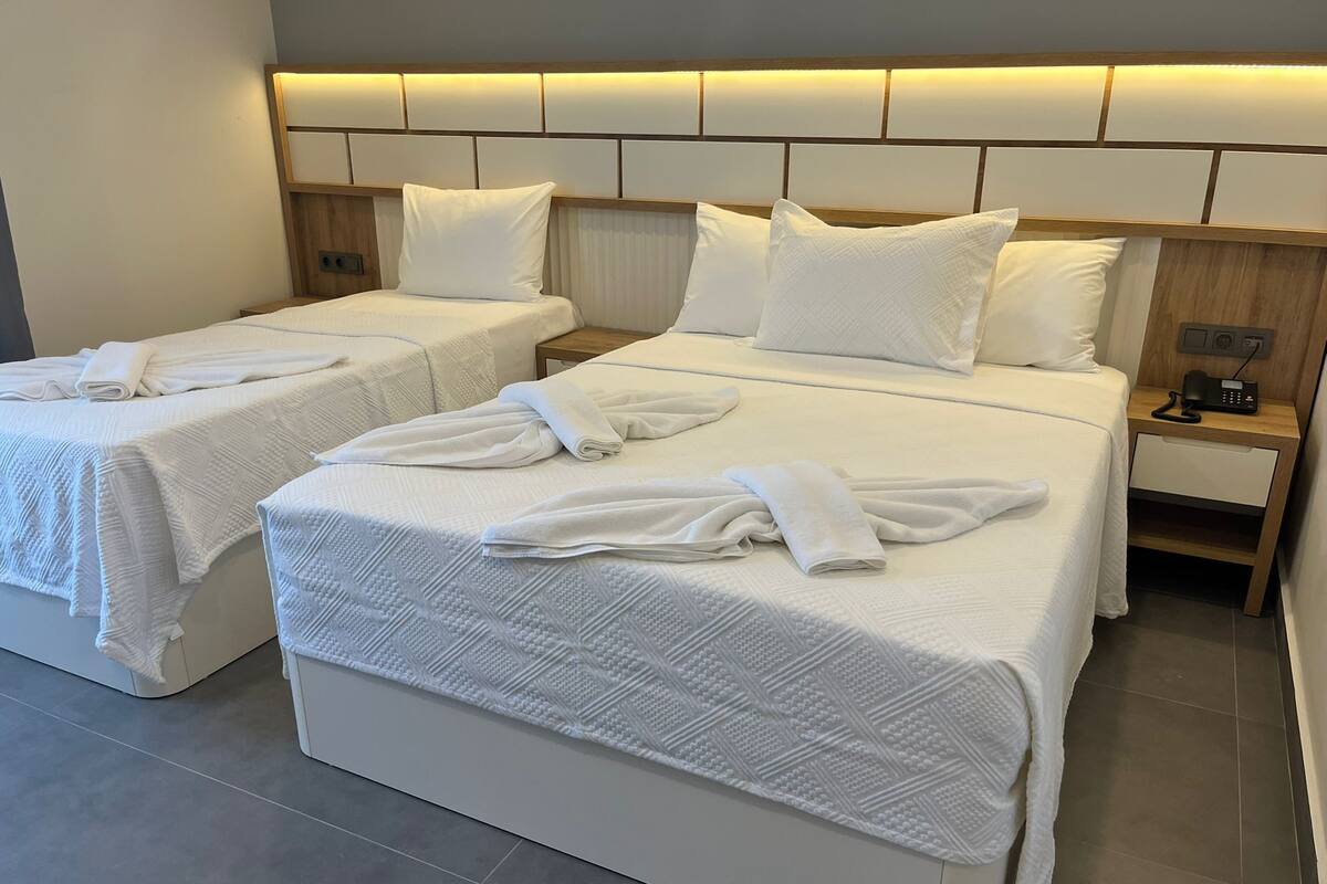 A hotel room with two beds, each with a headboard, white linens, and towels. There is a nightstand with a phone and a small drawer.