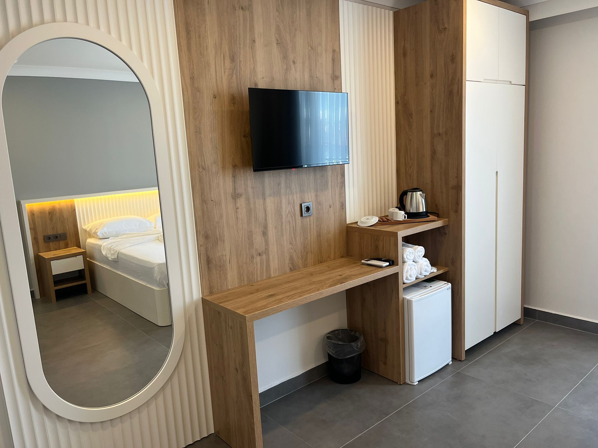 A modern hotel room with a wooden desk, a television, a small refrigerator, and a bed with a headboard.