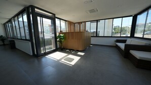 A modern interior with large windows, a reception desk, a seating area, and a potted plant. - Ege Vadi Otel (Ayvalik)