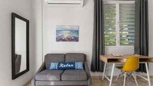 A modern living space with a grey sofa, a wooden desk, a yellow chair, and a painting on the wall. - Dowtown Studio Walkable to Town and Beach (Rincon)