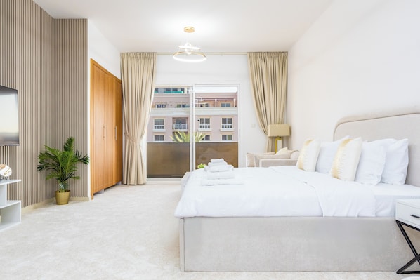 A hotel room with a bed, a TV, a desk, and a potted plant.