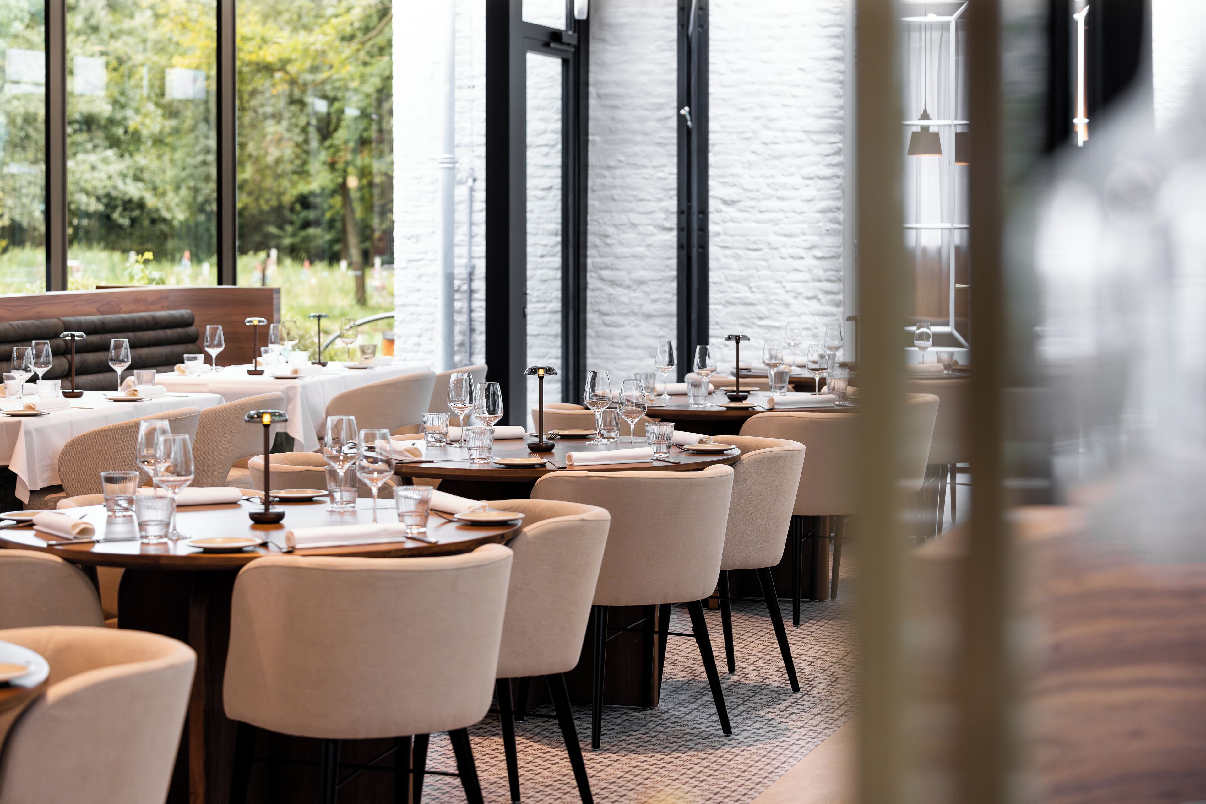 Un ristorante con diversi tavoli apparecchiati per mangiare, ampie finestre e vista sul verde circostante.