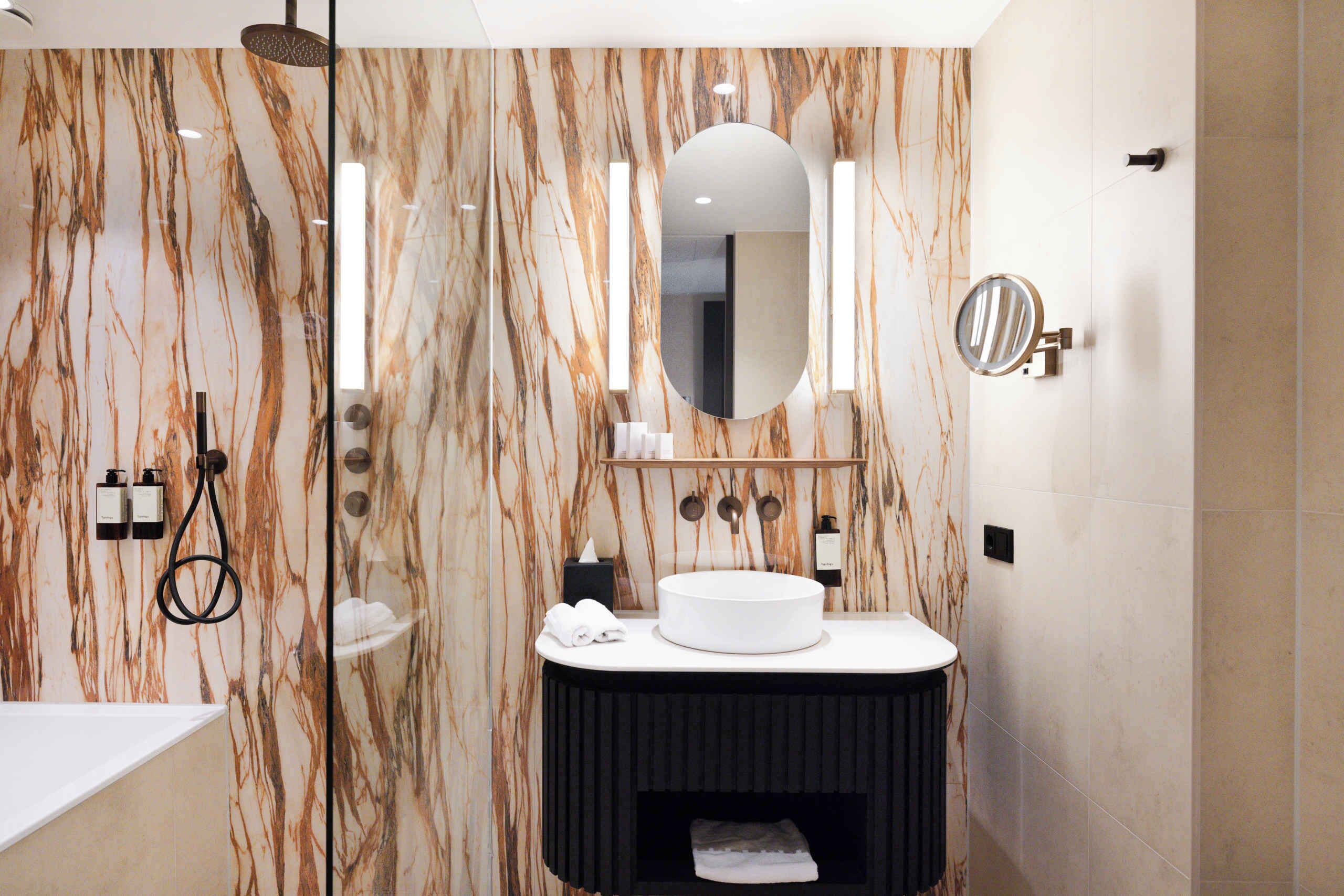 A modern bathroom with a marble wall, a round sink, a mirror, and a handheld showerhead.