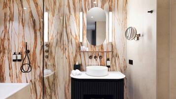 A modern bathroom with a marble wall, a round sink, a mirror, and a handheld showerhead.