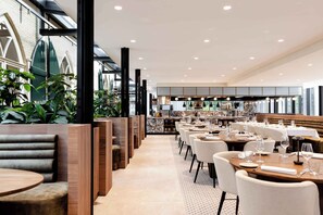 Un restaurante con cabinas de madera, mesas blancas y una cocina al fondo.