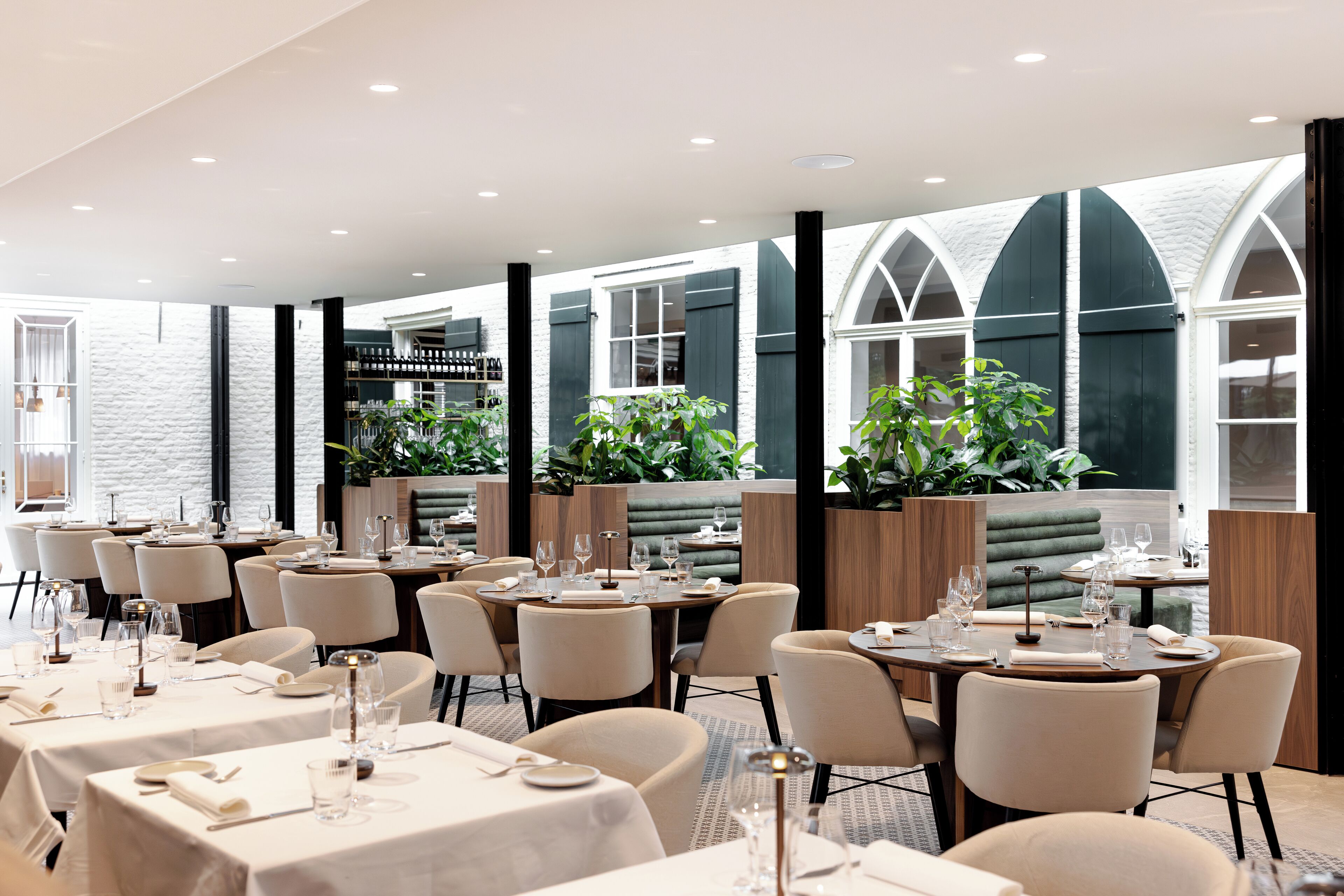 A modern restaurant with round tables, white tablecloths, and green plants.