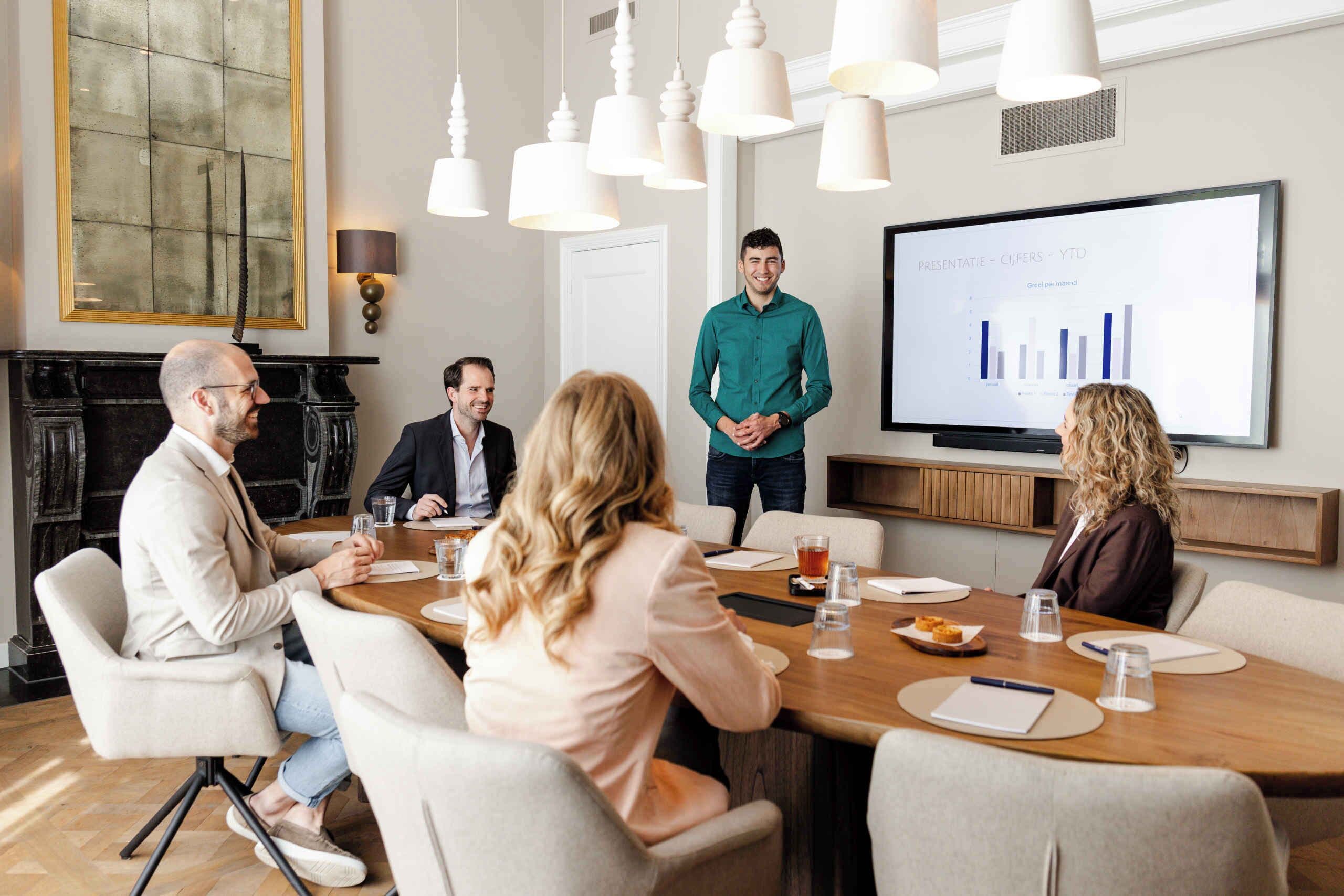 A conference room with a large screen displaying a presentation, a fireplace, and modern lighting fixtures.