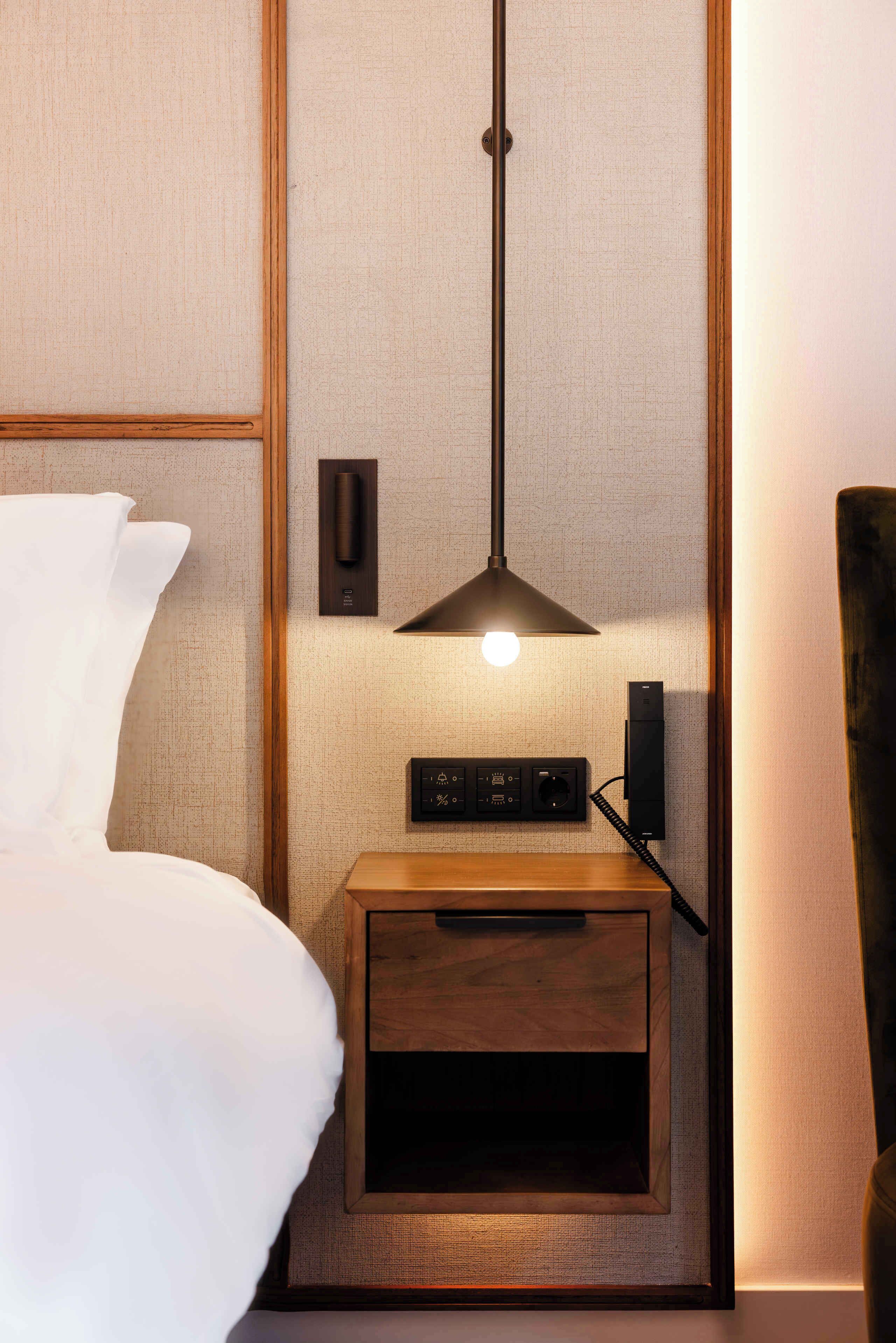 A neatly made hotel room with a bed, a bedside table with a lamp, and a small wooden cabinet.