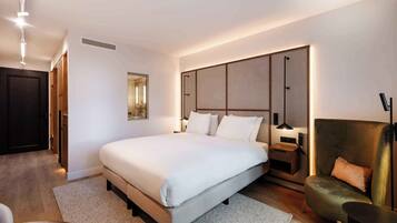 A modern bedroom with a large bed, bedside tables, a desk, and a green armchair.