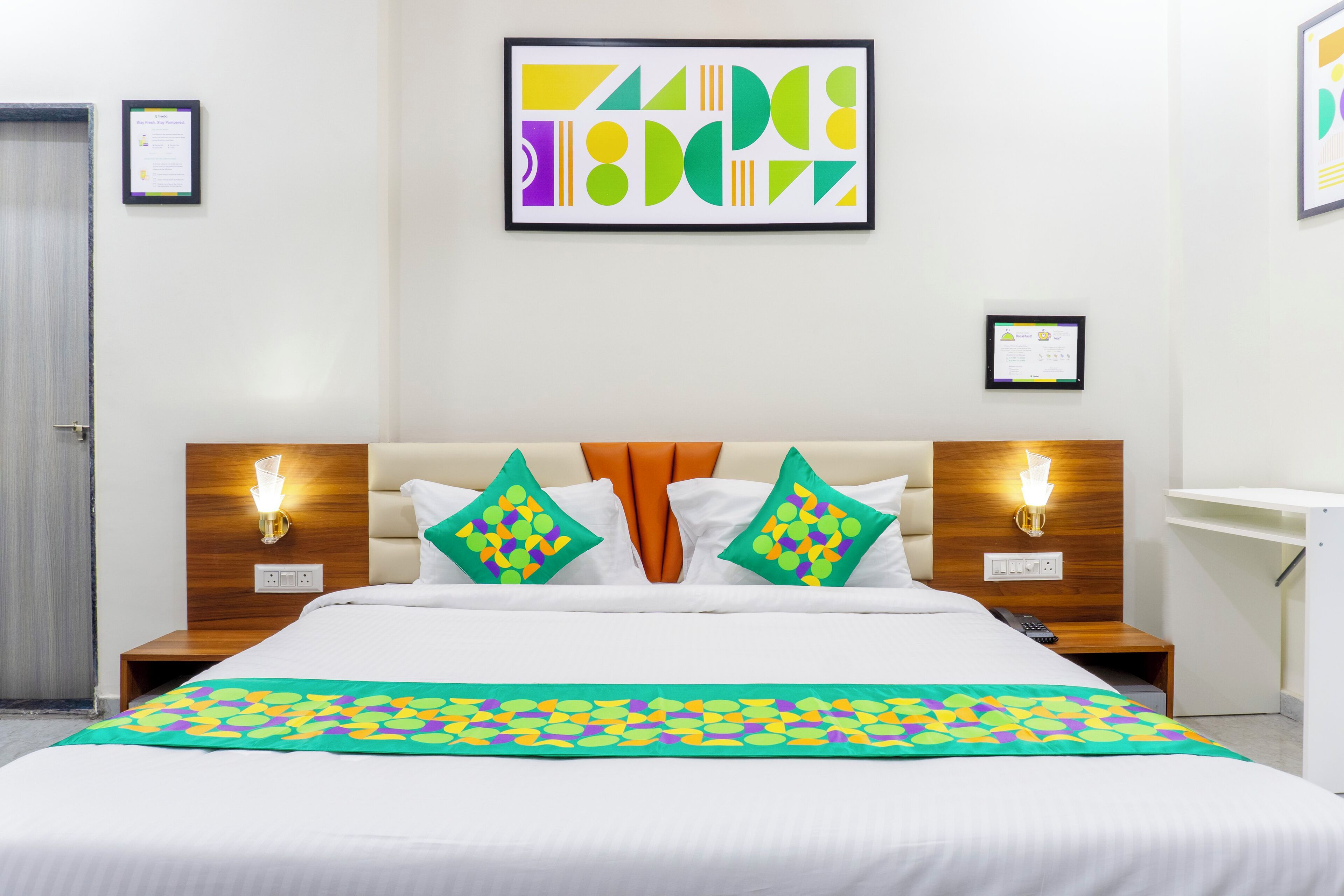 A hotel room with a large bed, two nightstands, a wooden headboard, and a colorful abstract painting on the wall.