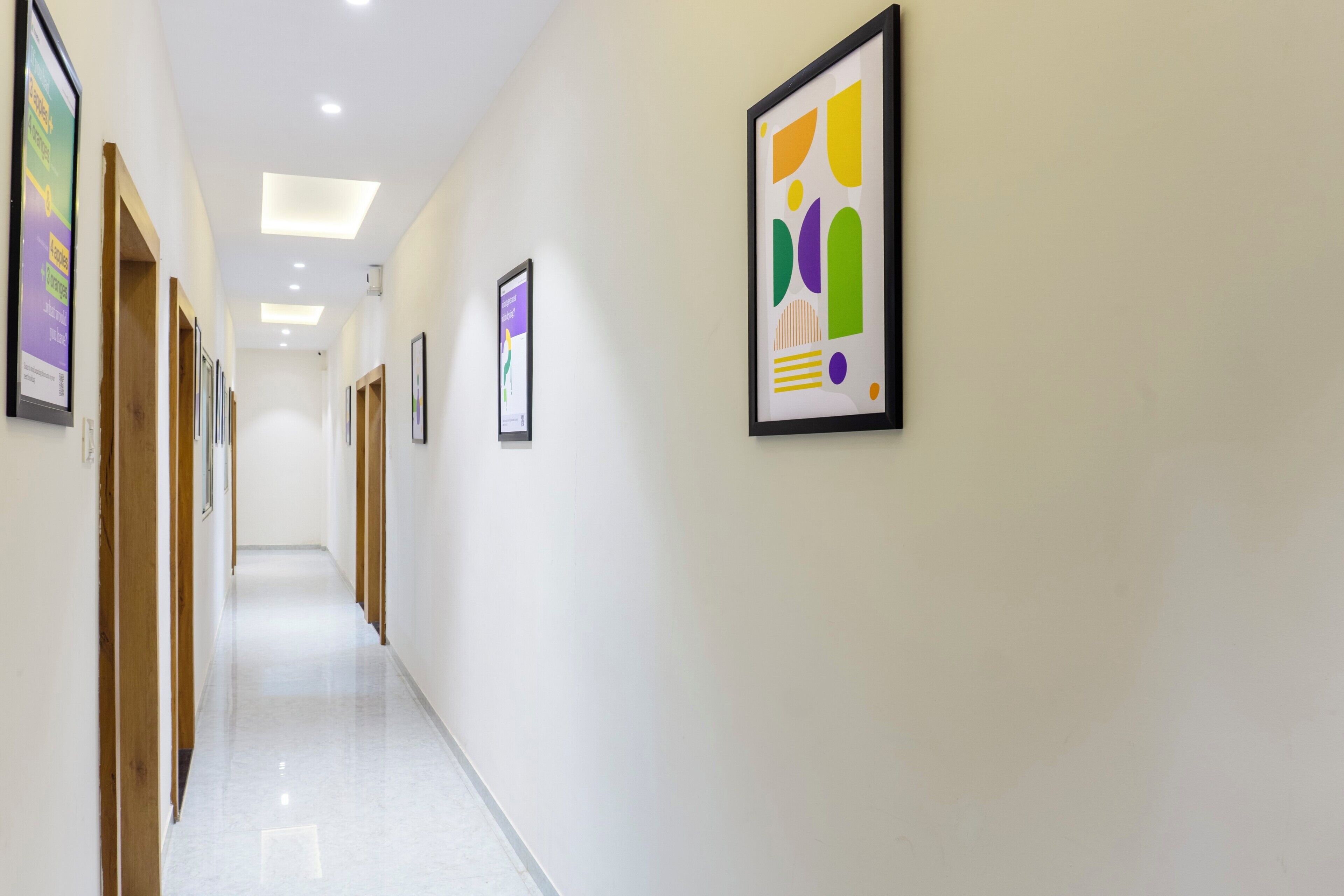 A hallway with framed artwork on the walls, wooden doors, and a white floor.