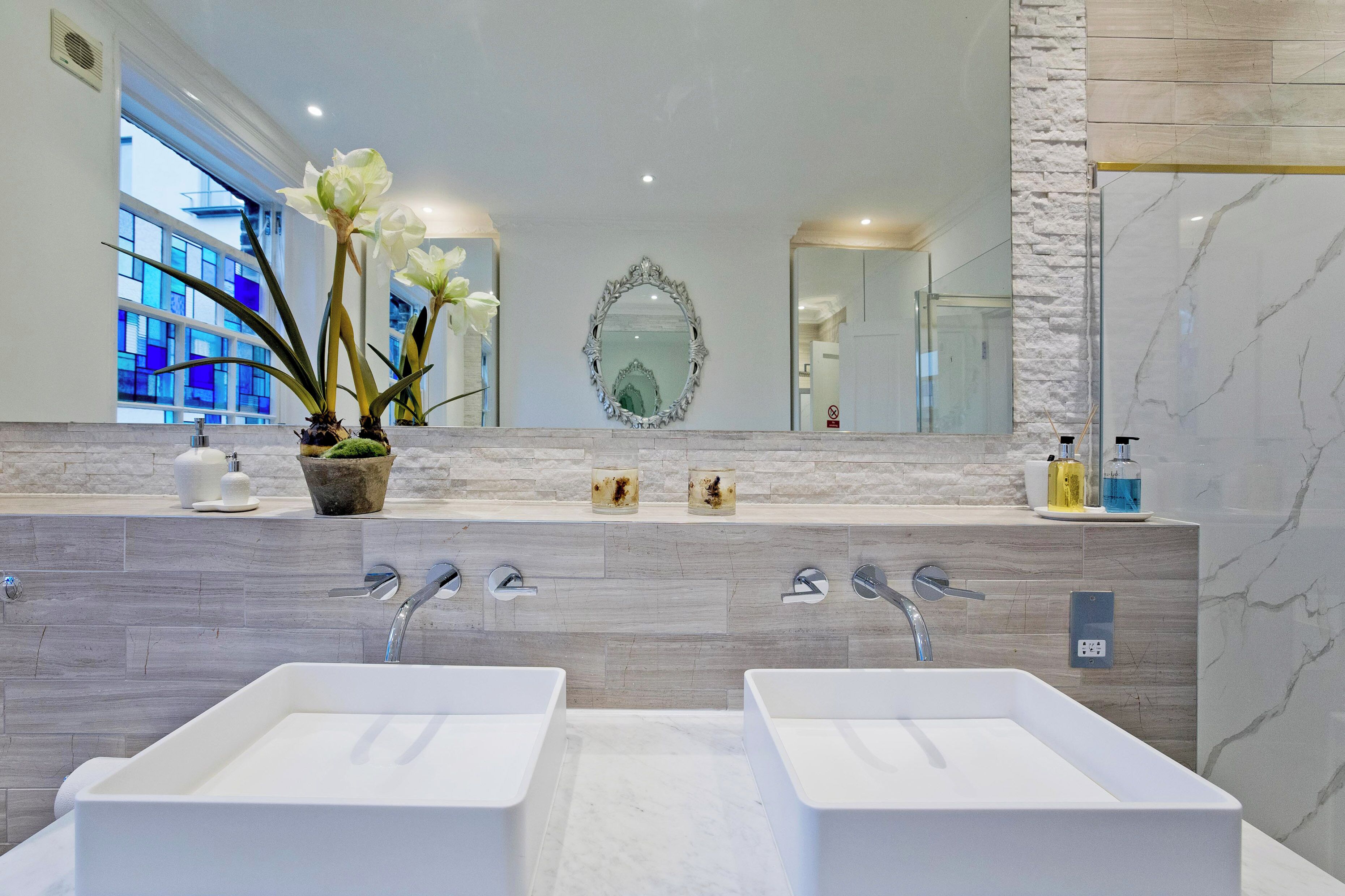 Un baño moderno con dos lavamanos, un espejo grande y una planta en maceta.