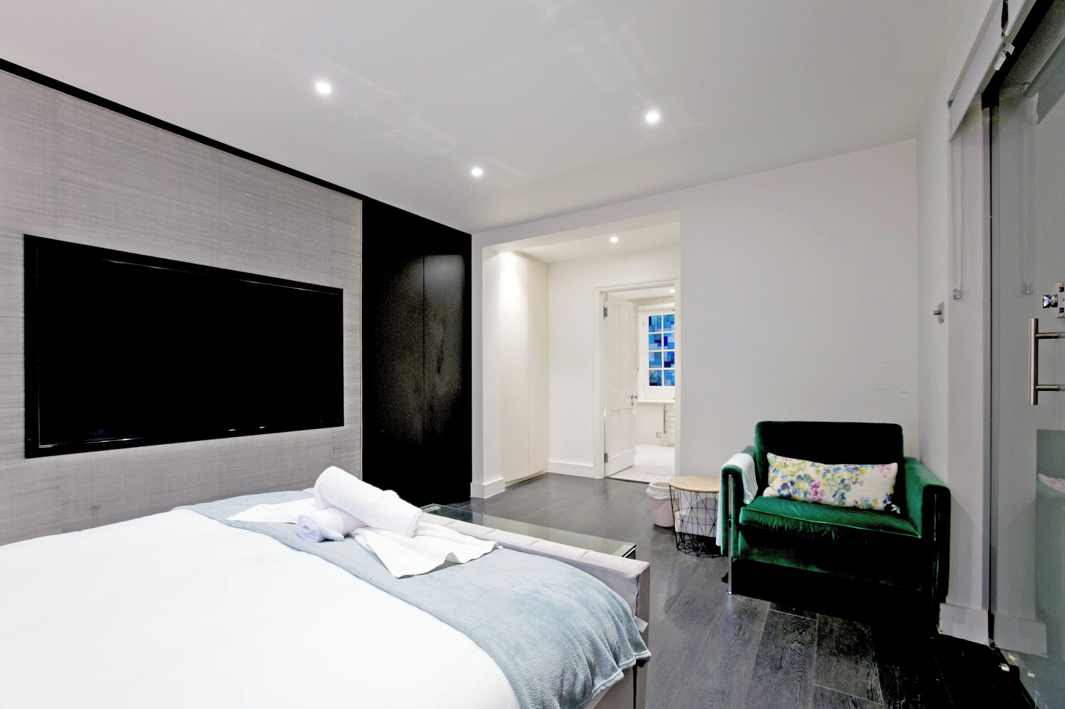 Ein modernes Hotelzimmer mit einem großen Bett, einem flachbildfernseher an der Wand, einem grünen Sessel und einem kleinen Tisch mit einer Lampe.