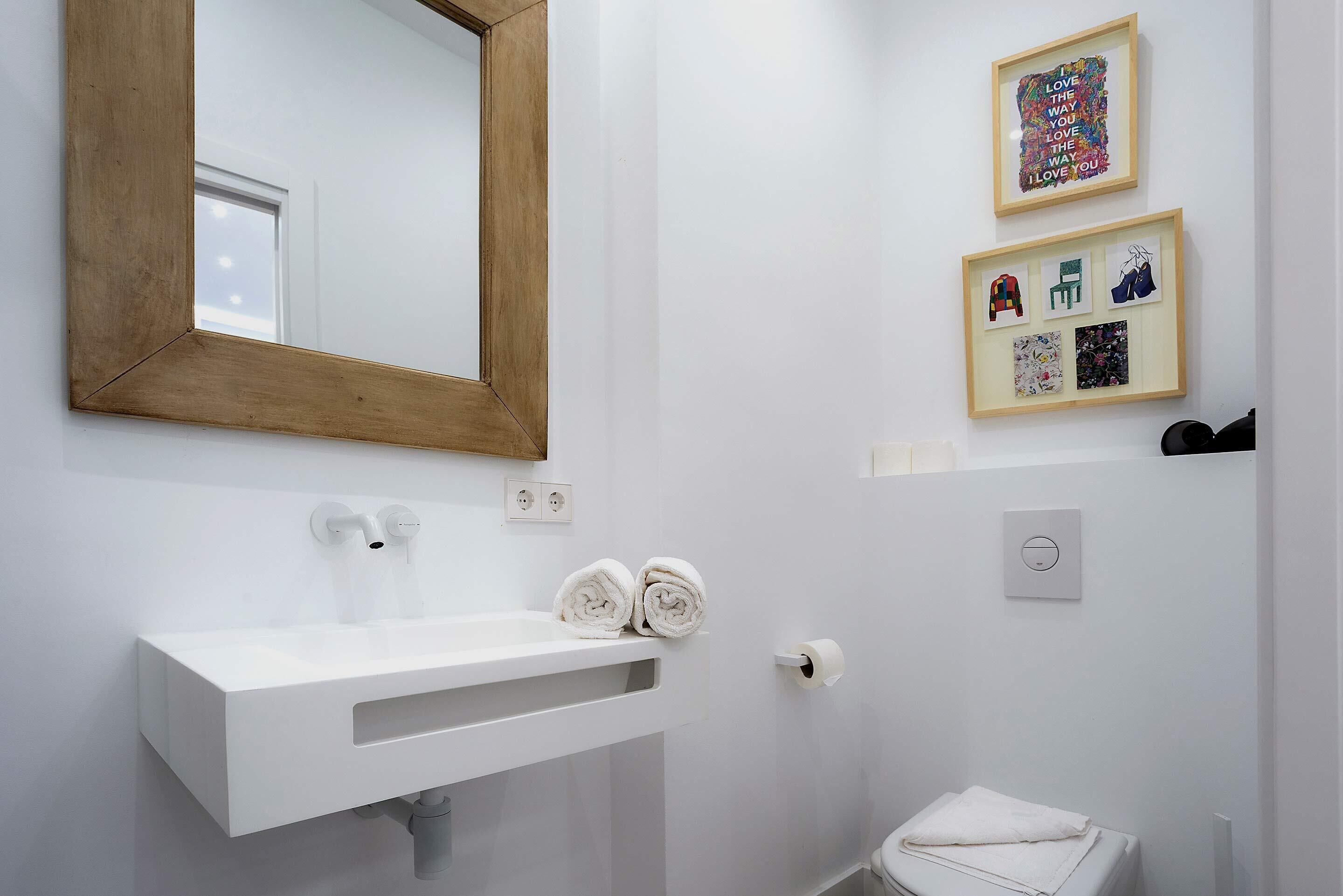 Un bagno moderno con un lavandino bianco, uno specchio con cornice in legno e opere d'arte appese alla parete.