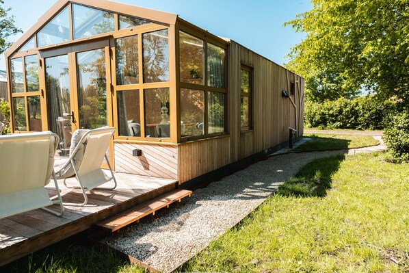 A modern wooden structure with large windows, a wooden deck, and outdoor seating.