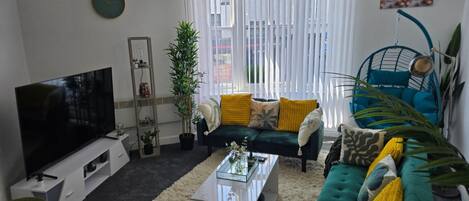 A living room with a sofa, coffee table, TV, and a plant.