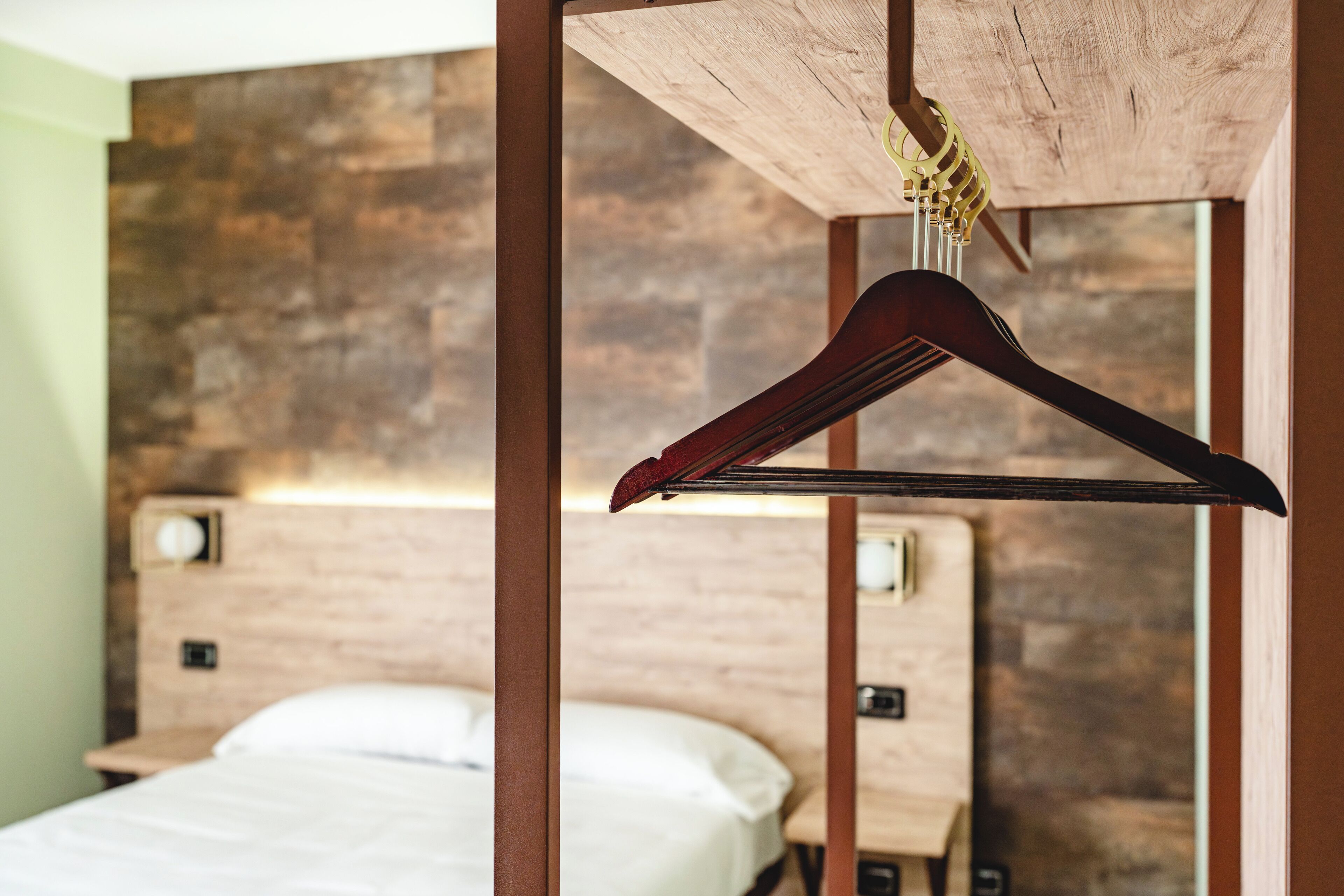 A bedroom with a wooden headboard, a hanging wooden hanger, and a bed with white bedding.