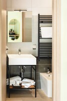Un baño moderno con un lavamanos blanco, un espejo, un perchero para toallas y una bañera.