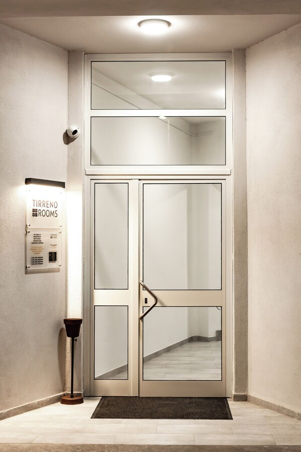 Puertas dobles con un panel de vidrio, un letrero que dice 'Tirreno Rooms' y una lámpara de pie.
