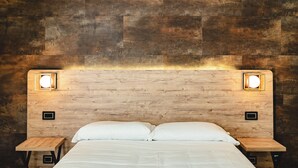 A bed with white linens, two bedside tables, and a wooden headboard with two wall-mounted lights. - CODE ROOMS by Hotel Villa Tirreno (Tarquinia)