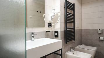 A modern bathroom with a white sink, a black towel rack, a glass shower enclosure, and a bidet.