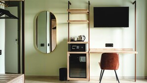 A modern room with a wooden desk, a flat-screen TV, a round mirror, and a compact storage unit with a microwave. - CODE ROOMS by Hotel Villa Tirreno (Tarquinia)