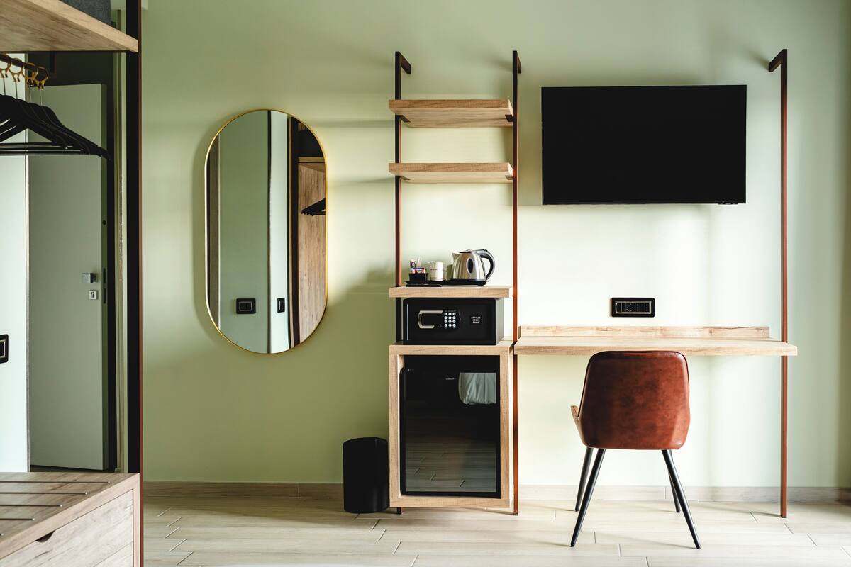 A modern room with a wooden desk, a flat-screen TV, a round mirror, and a compact storage unit with a microwave.