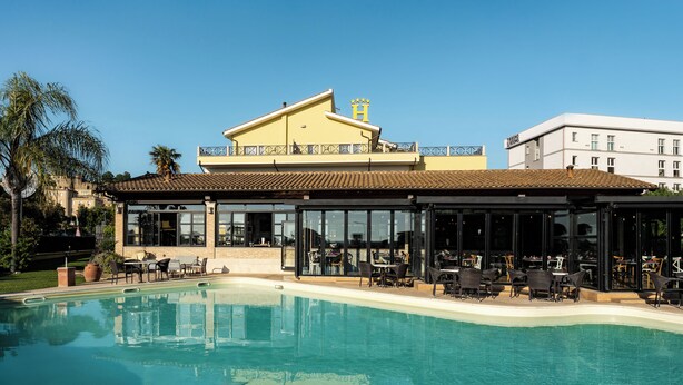 A hotel with a pool, outdoor seating, and a yellow building with a 'H' sign. - CODE ROOMS by Hotel Villa Tirreno (Tarquinia)