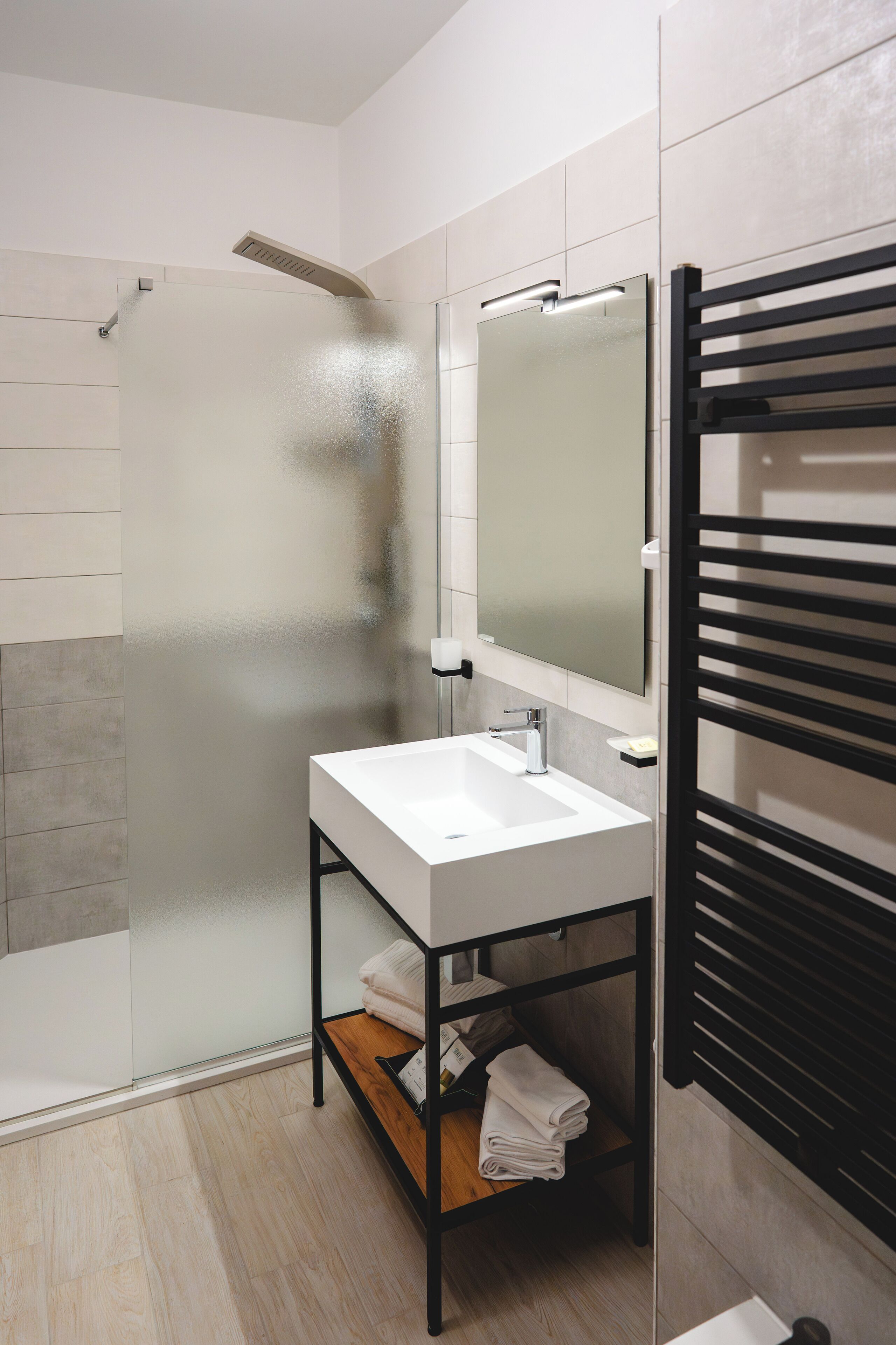 Un baño moderno con cabina de ducha de vidrio, un lavamanos blanco con marco negro y un toallero negro.