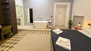 A modern bedroom with a large bed, a bathtub, and a vanity with a mirror. - LA PIAZZA SUITE (Naples)