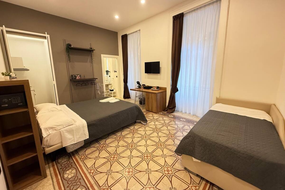 A hotel room with two beds, a desk, a TV, and a shower area.