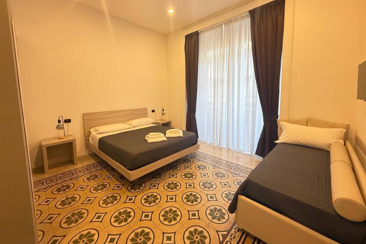 A hotel room with a bed, a bedside table, a lamp, a chair, and a window with curtains.