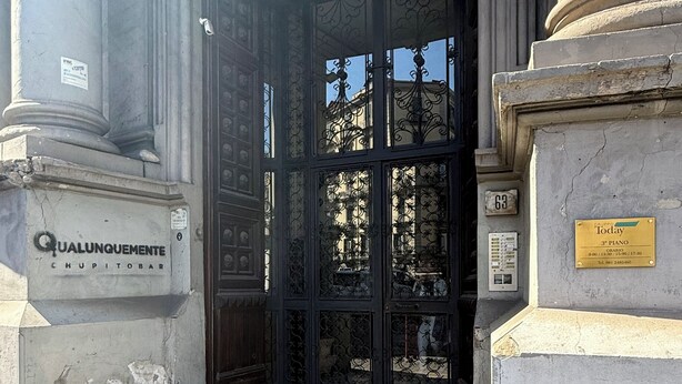 A building entrance with a metal gate, a sign reading "QUALUNQUEMENTE CHUPITOBAR", and a plaque indicating "3rd Piano". - LA PIAZZA SUITE (Naples)