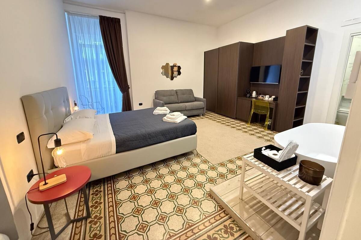 A hotel room with a bed, a sofa, a desk, a TV, and a bathroom.