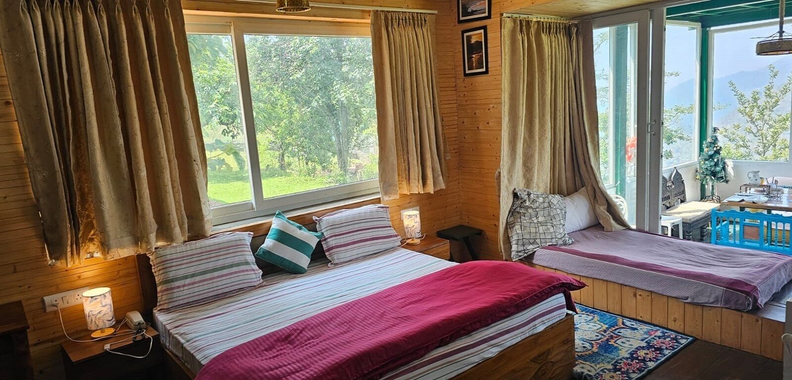 Una habitación acogedora con dos camas, ventanas amplias, una mesita y vistas al verdor exterior.