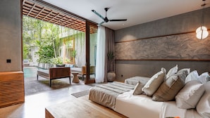 A modern bedroom with a large bed, a wooden bench, and a view of an outdoor pool area. - Vinaka Villa By Betterplace (Canggu)