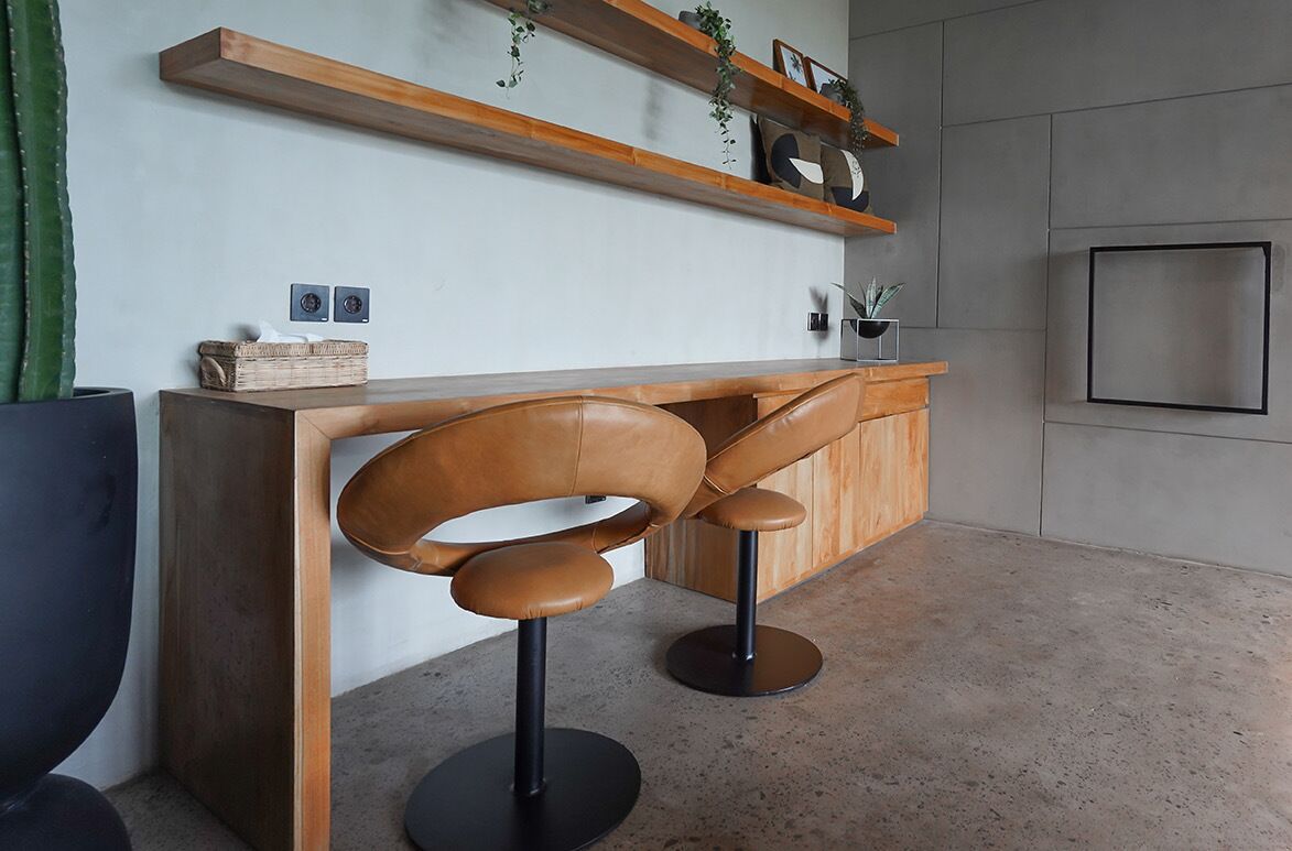 A modern kitchen with a wooden countertop, two bar stools, and a hanging shelf with decorative items.