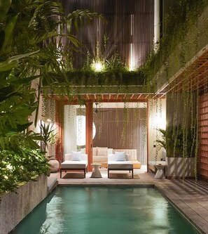 Uma área de piscina interna com duas espreguiçadeiras, uma mesinha e um espaço de estar com almofadas.