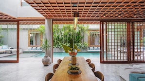 A spacious indoor area with a wooden dining table, chairs, and a view of a swimming pool. - Vinaka Villa By Betterplace (Canggu)