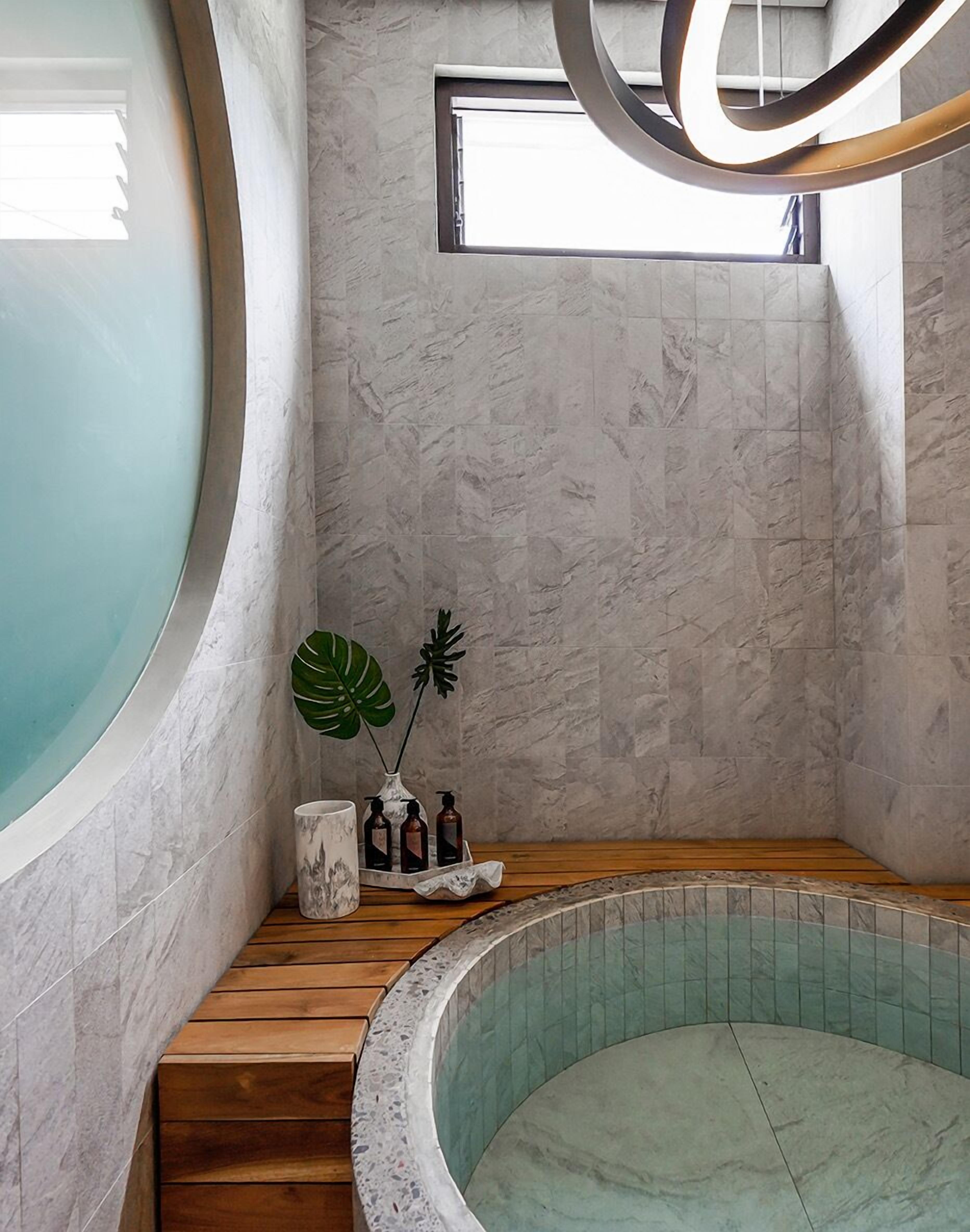 A spa room with a curved wooden bench, a small seating area with a plant, and a large window.