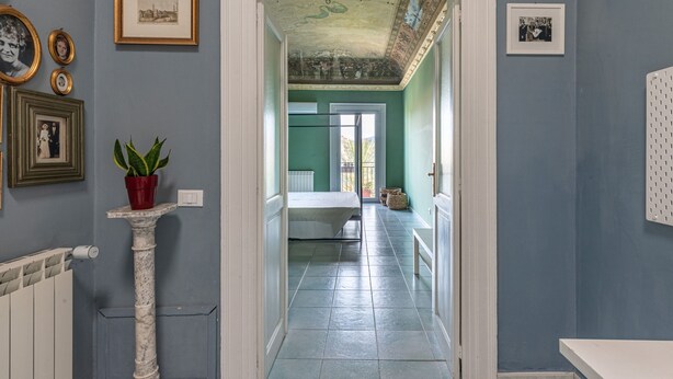 A hallway with a white column, a potted plant, and framed pictures on the wall. - Casa Garibaldi in Piazza by Wonderful Italy (Palermo)