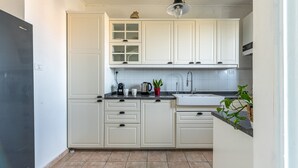 A kitchen with white cabinets, a black countertop, a sink, a coffee maker, a kettle, and a potted plant. - Casa Garibaldi in Piazza by Wonderful Italy (Palermo)